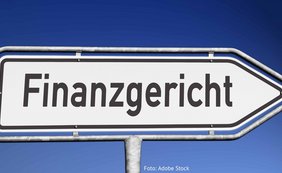 vor dunkelblauem Hintergrund steht das Wort "Finanzgericht" auf einem Verkehrsschild, das nach rechts weist