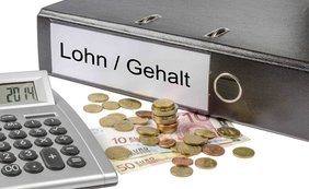 Schwarzer Aktenordner mit der Aufschrift „Lohn/Gehalt“; daneben liegt ein Taschenrechner, Euro-Geldscheine und Münzen. 