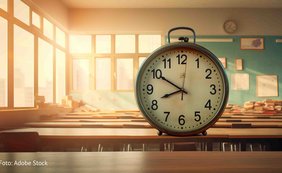 große Wanduhr auf einer Schulbank in weichem Licht