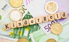 Euromünzen liegen auf Geldscheinen, darauf ist aus Würfeln das Wort Kindergeld gelegt