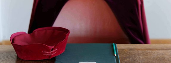 auf der Richterbank liegen Barett und Arbeitsmappe, dahinter ein Richterstuhl, auf dem eine Robe hängt