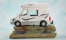 Weißes Wohnmobil-Modell, das auf einem hohen Stapel von Geldscheinen steht. 