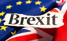 Das Bild zeigt das Wort „Brexit“ auf einem zerrissenen Papier über den Flaggen der EU und des Vereinigten Königreichs.