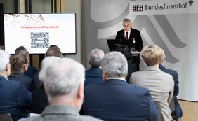 Zuschauer sieht man von hinten, der Präsident des Bundesfinanzhofs steht am Rednerpult