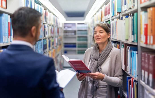 zwei Personen im Gespräch zwischen Regalen in Bibliothek des Bundesfinanzhofs